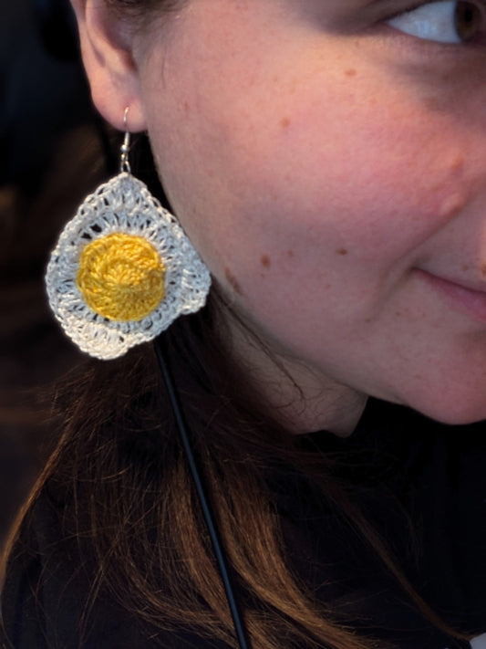 A girl smiling while wearing a playful crochet fried egg earring, showcasing her unique and fun style
